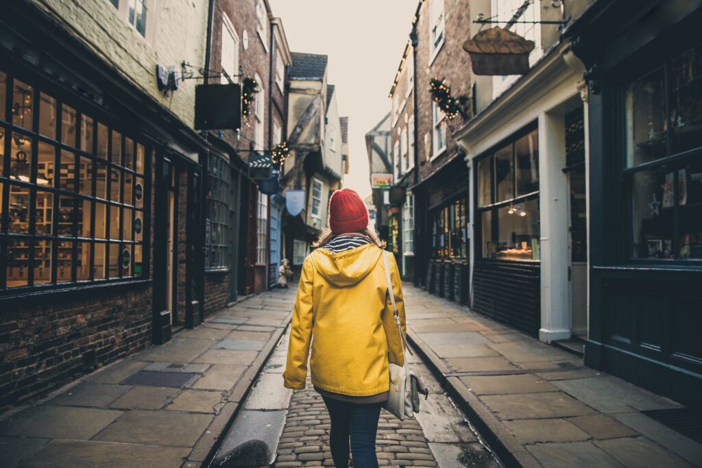 A rear view of a girl in a yellow coat walking along the historic street known as The Shambles in York, UK